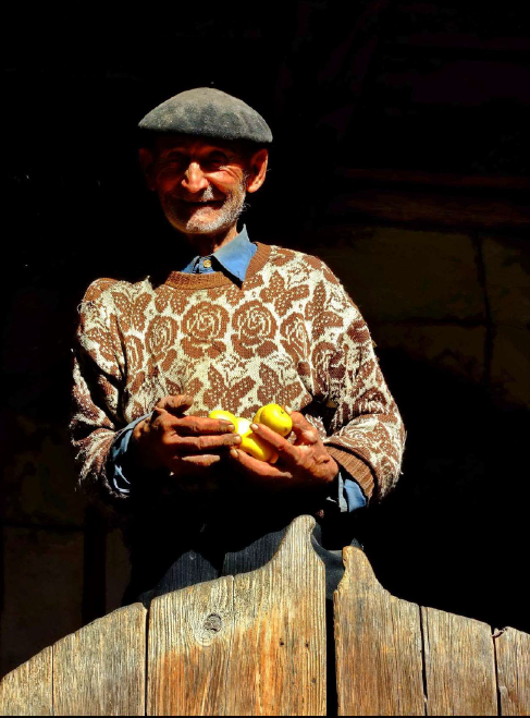 Farmer wearing a floral sweater and a hat holding lemons, fresh produce