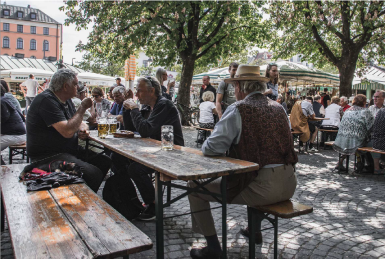 A group of people enjoying beer in Munich's beer garden while sitting on a bench and table