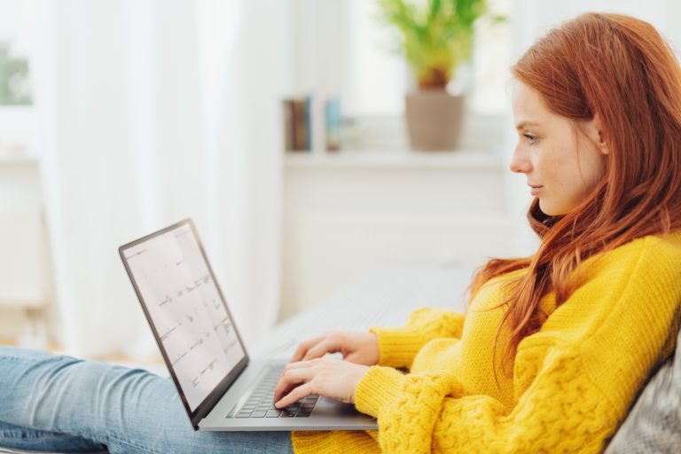 Young redhead woman using her laptop at home online shopping in yellow sweater